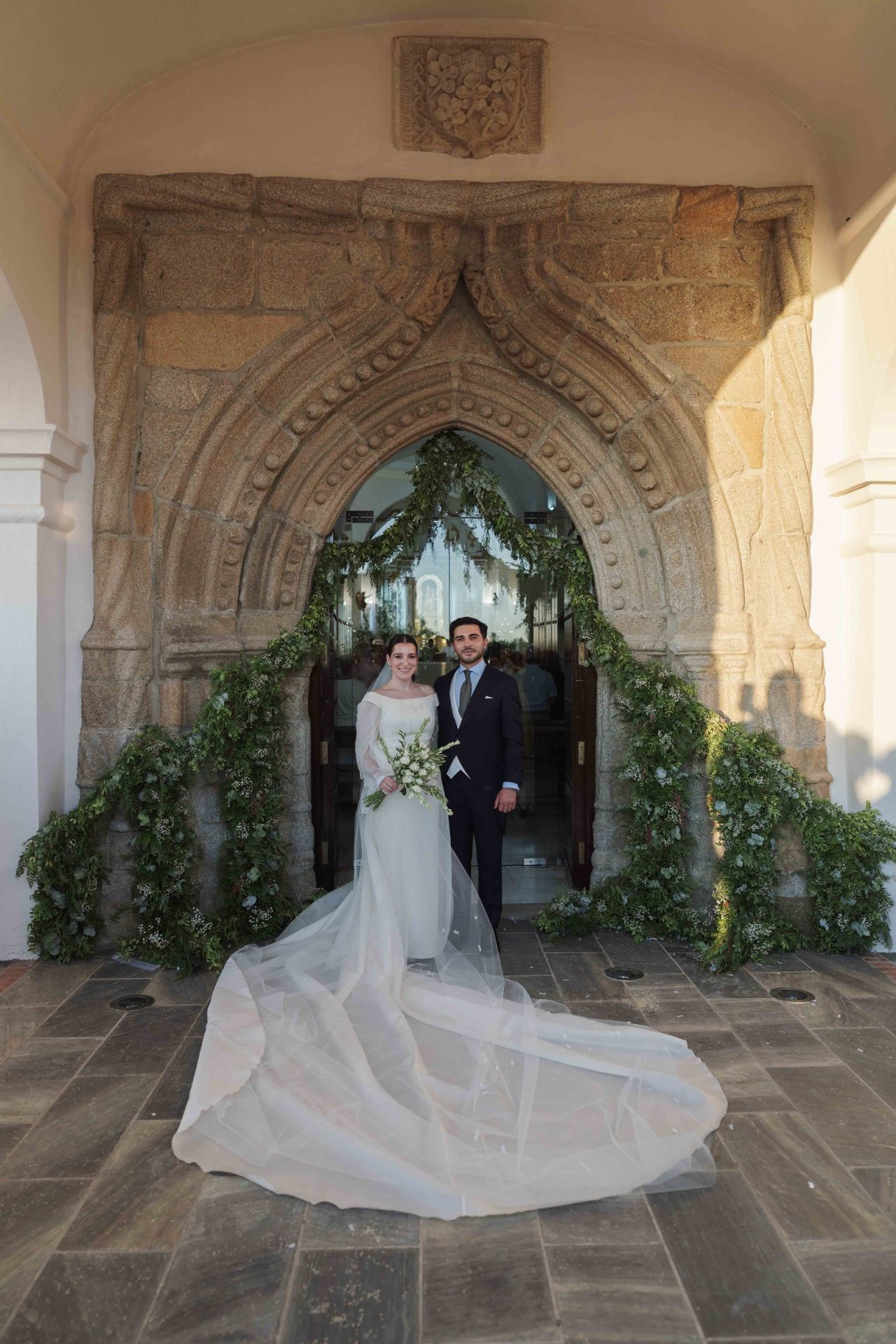Inmaculada y Jesús en la puerta del Santuario de Nuestra Señora de Gracia, con su vestido de novia exclusivo y la cola de gazar de seda natural